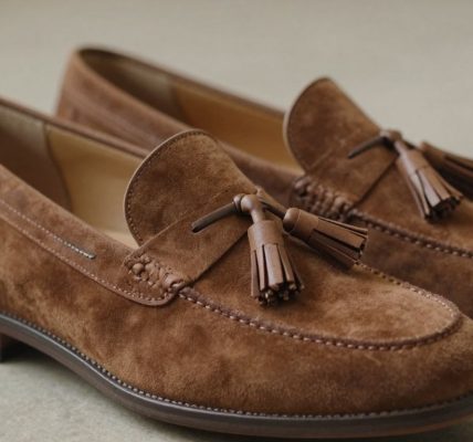 Brown suede tassel loafers on a textured surface.
